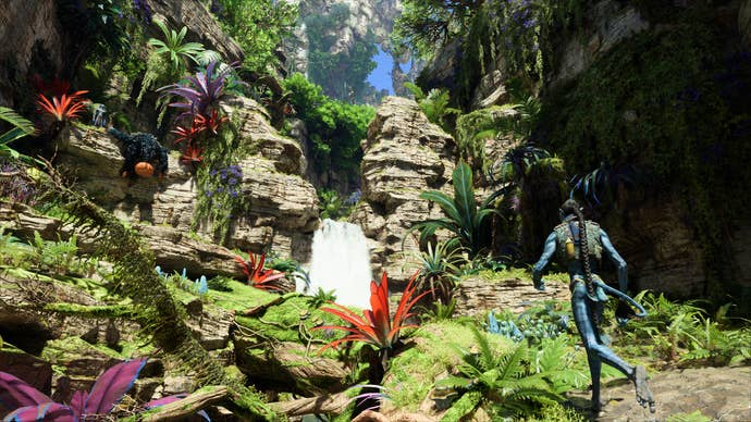Avatar : Frontiers of Pandora : une cascade dans une jungle, des couleurs vibrantes, des verts riches et des rouges profonds, alors qu'un Na'vi admire le paysage.